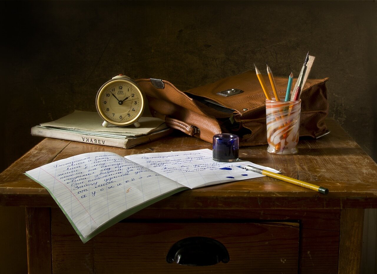 机の上に置かれたノートと時計と文房具の画像