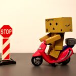 段ボールでできたロボットがバイクに乗って、「STOP」の標識で止まっている画像