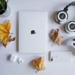 机にmacbook, プレステのコントローラー、ヘッドフォン、スマホが置かれている画像